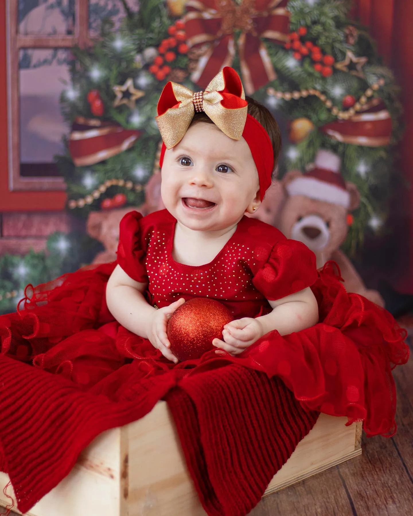 Bebê de vestido vermelho sentada em cenário natalino