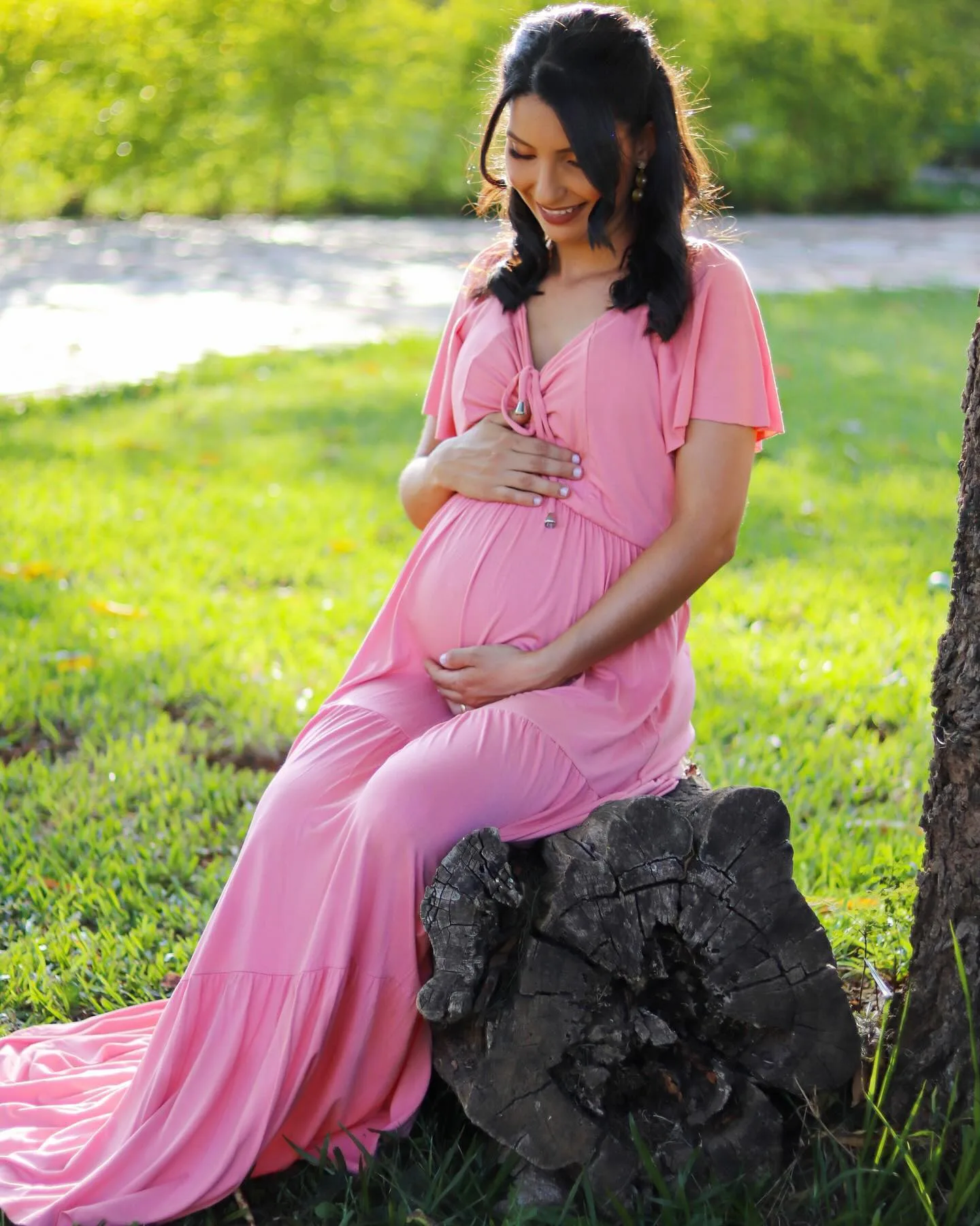 Gestante de vestido rosa sentada junto a uma árvore, em área verde