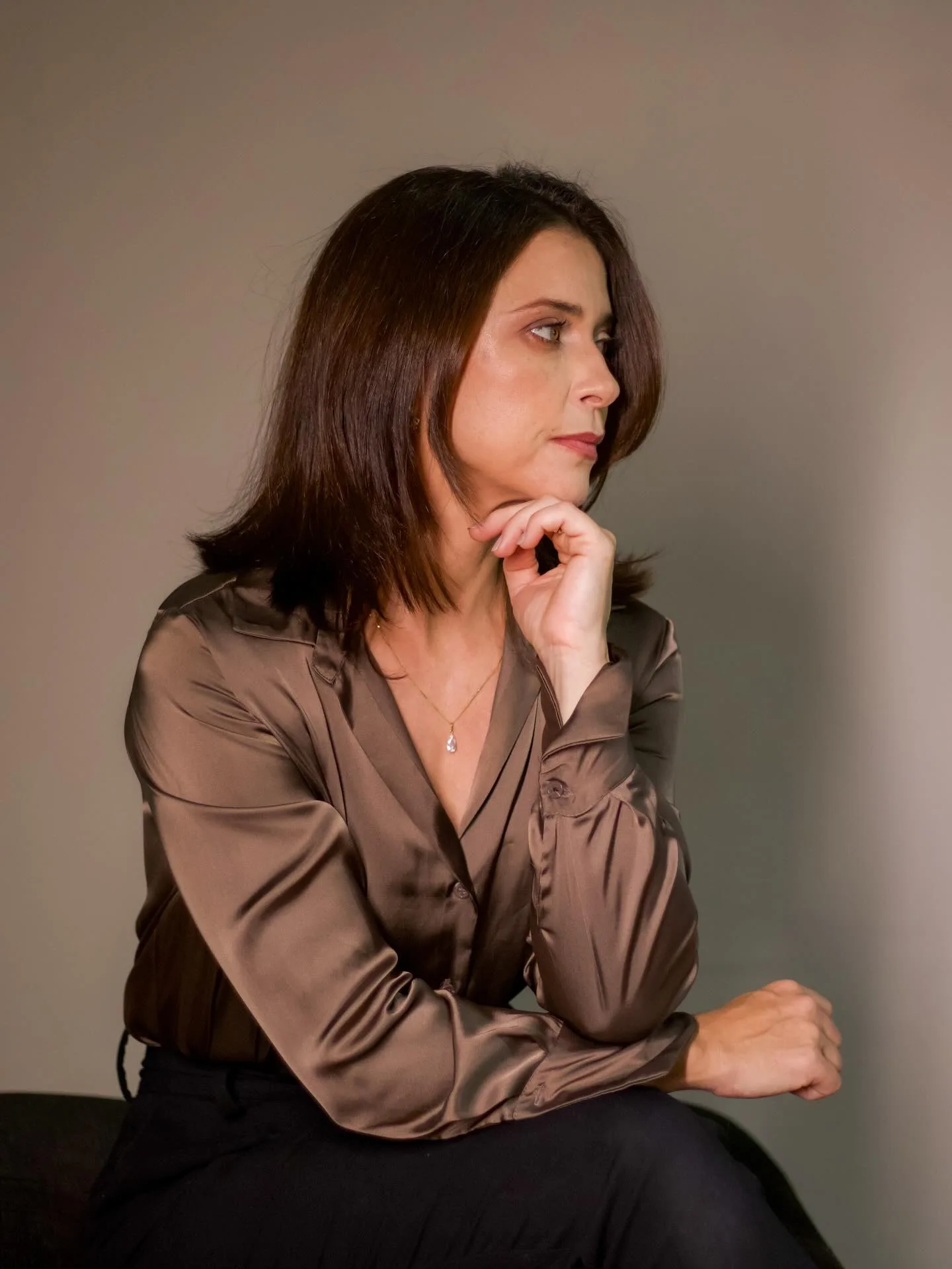 Mulher de camisa marrom sentada de perfil em ambiente interno
