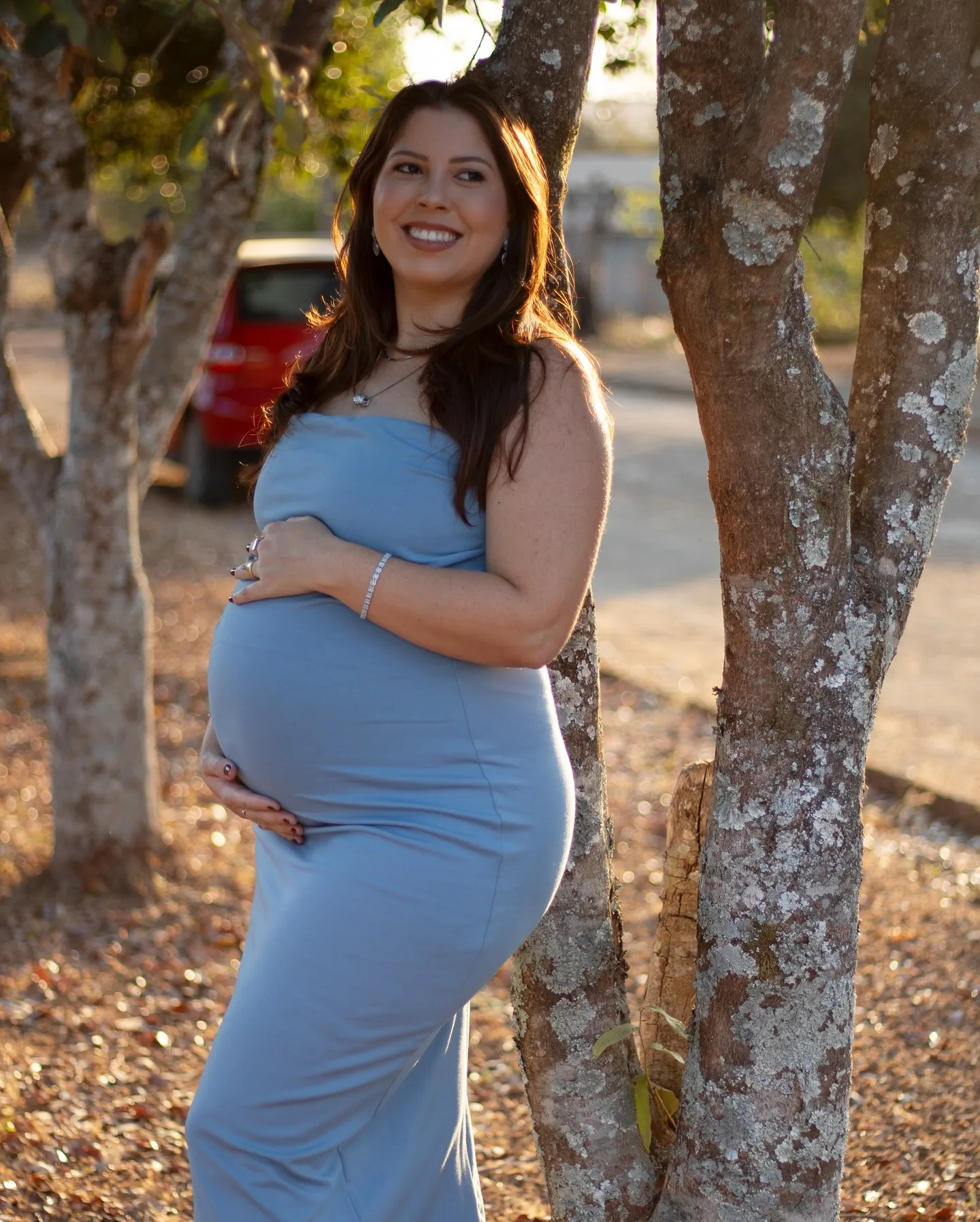 Gestante de vestido azul junto a uma árvore sob luz natural