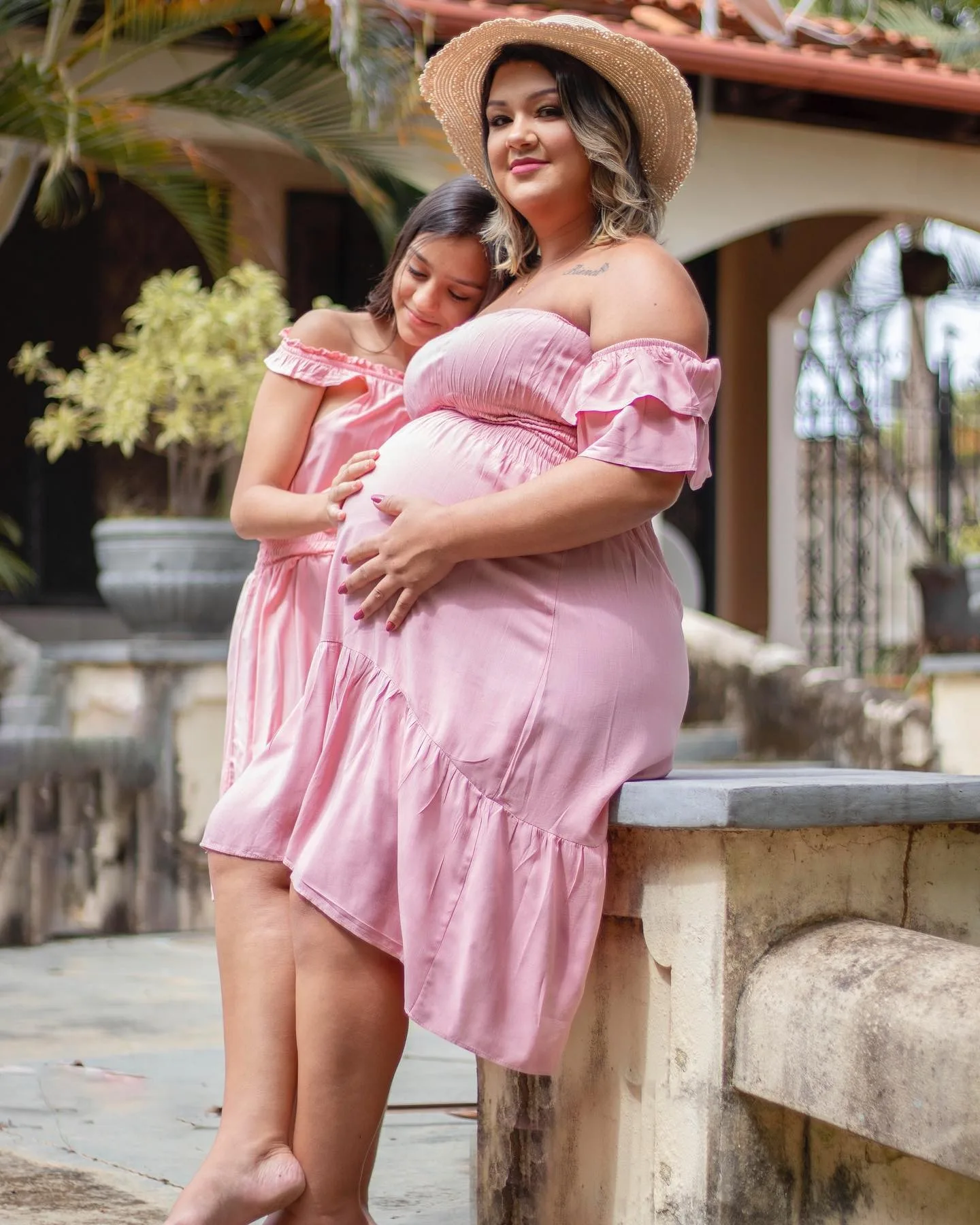 Gestante de vestido rosa abraça uma menina em um jardim